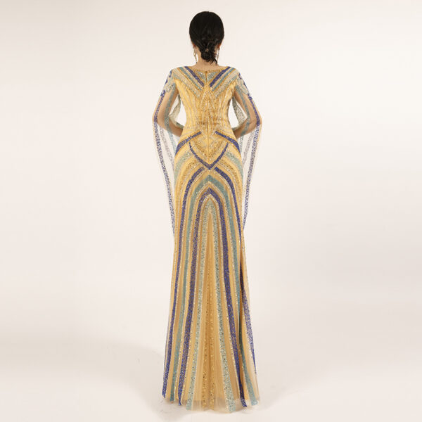 Step into the spotlight with this showstopping gold evening gown, where luxury meets artistry. Hand-sewn beading in bold geometric arches adorns the entire gown, catching the light with every step to create a dazzling, multi-dimensional effect. The sheer cape sleeves float gracefully from the shoulders, adding a romantic, weightless touch to the structured mermaid silhouette. The V-neckline frames the collarbone beautifully, while the rich gold base provides a warm, opulent backdrop to the cool blue and turquoise beadwork—ideal for the bride, gala attendee, or anyone looking to exude confidence and glamour.