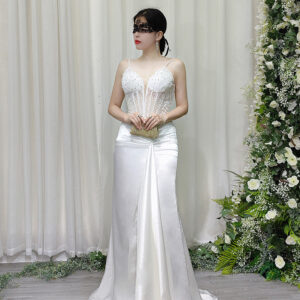 White beaded spaghetti strap mermaid gown with sheer corset bodice and satin skirt, worn with a lace mask and beaded clutch.
