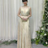 Champagne gold pleated halter gown with deep V-neck, beaded waistband, and flowing floor-length skirt, worn with a lace mask and beaded clutch.