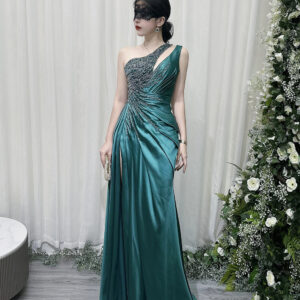 Emerald green one-shoulder satin mermaid gown with beaded bodice, high slit, and trailing train, styled with a lace mask and beaded clutch.