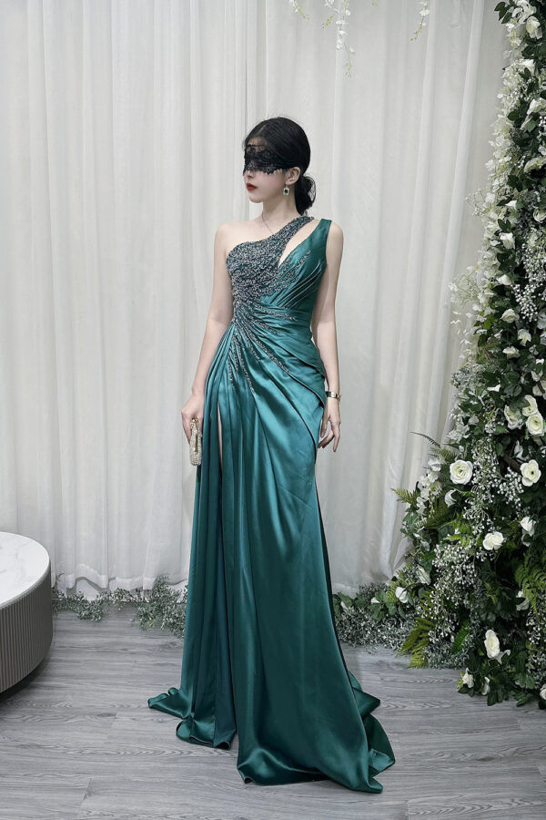Emerald green one-shoulder satin mermaid gown with beaded bodice, high slit, and trailing train, styled with a lace mask and beaded clutch.