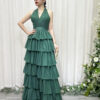 Emerald green halter-neck tiered ruffle gown with glittery fabric and trailing train, styled with a lace mask and beaded clutch.