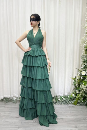 Emerald green halter-neck tiered ruffle gown with glittery fabric and trailing train, styled with a lace mask and beaded clutch.