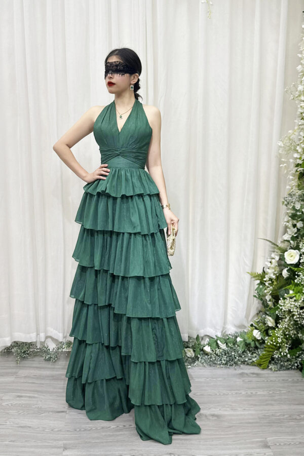 Emerald green halter-neck tiered ruffle gown with glittery fabric and trailing train, styled with a lace mask and beaded clutch.