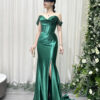 Emerald green off-the-shoulder satin mermaid gown with corset bodice, glittery neckline, high slit, and trailing train, styled with a lace mask and beaded clutch.