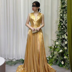 Stunning gold metallic pleated evening gown with deep V-neck, high slit, and sweeping train, worn with a black lace mask and beaded clutch.