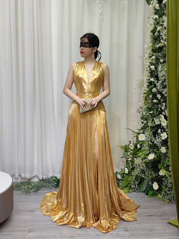 Stunning gold metallic pleated evening gown with deep V-neck, high slit, and sweeping train, worn with a black lace mask and beaded clutch.