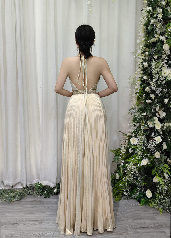Luxury champagne gold pleated halter gown with crystal-embellished waistband and flowing skirt.