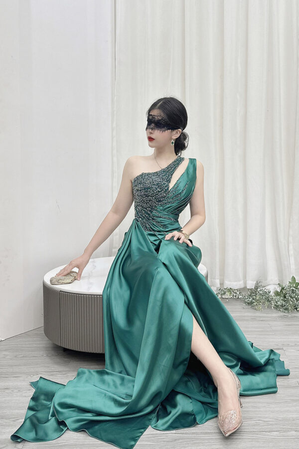 Modern emerald green one-shoulder satin gown with beaded detailing, high slit, and trailing train.