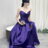 Modern purple strapless satin gown with ruched bodice, high slit, and trailing train, styled with a lace mask and beaded clutch.