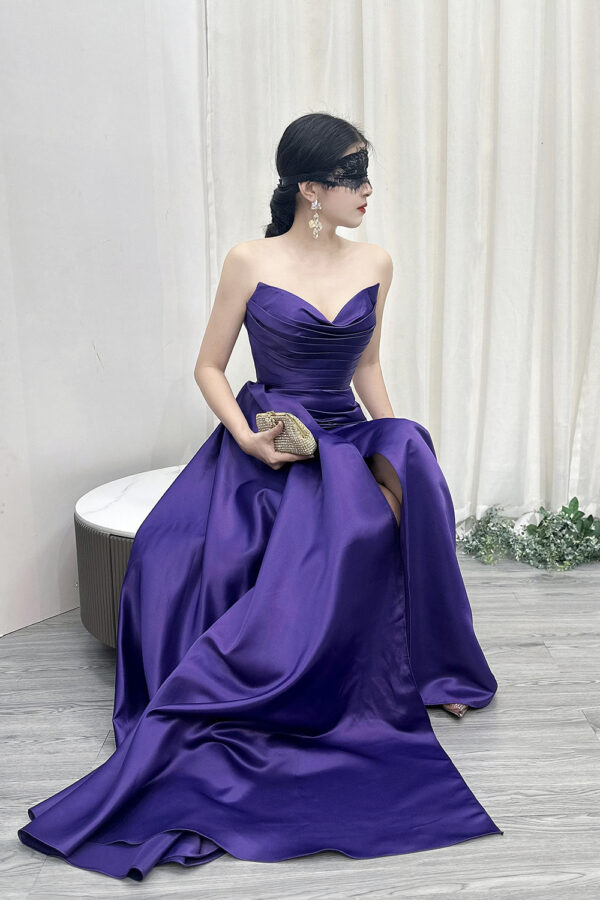 Modern purple strapless satin gown with ruched bodice, high slit, and trailing train, styled with a lace mask and beaded clutch.