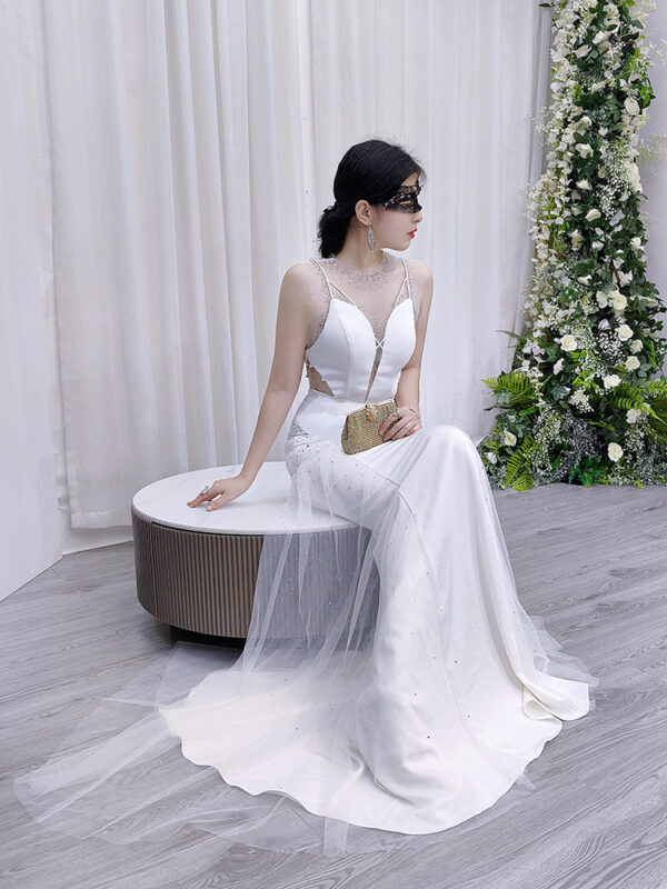 Modern white mermaid gown with sheer illusion neckline, side cutouts, and sparkling tulle train.