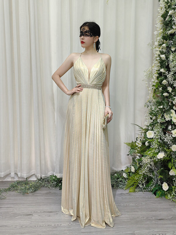 Romantic champagne pleated halter gown with deep V-neck and beaded waist, styled with a lace mask and beaded clutch.