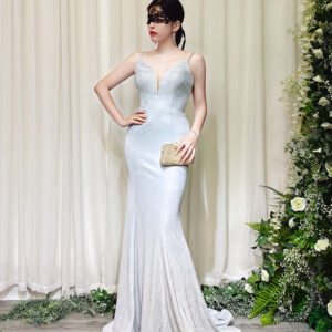 Elegant silver glitter mermaid evening gown with spaghetti straps and deep V-neck, worn by a woman in a black lace mask, holding a beaded clutch.