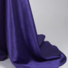 Dramatic deep purple off-the-shoulder satin floor-length gown with corset waist and flowing side train, red-carpet worthy formal wear.
